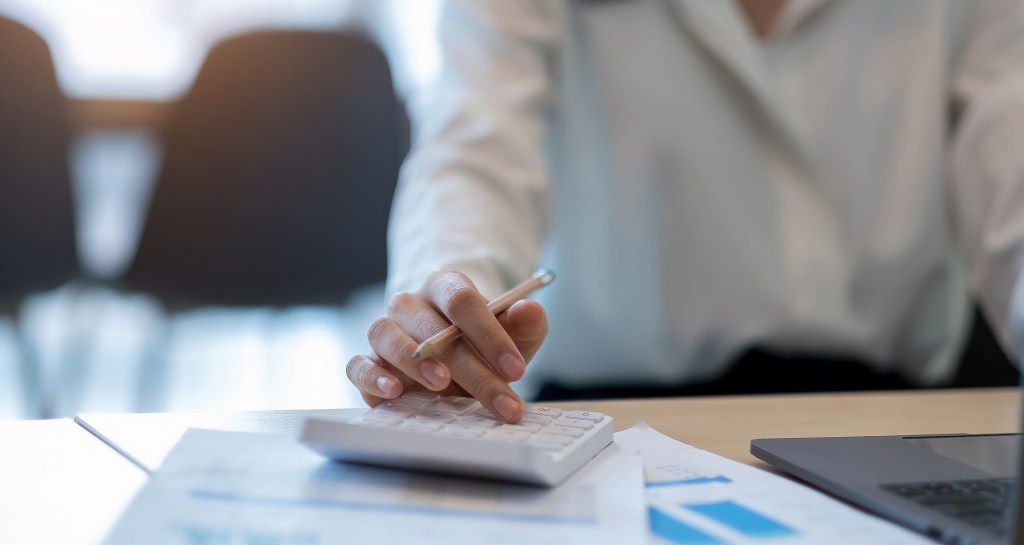 Close up Business woman using calculator and laptop for do math finance on wooden desk in office and business working background, tax, accounting, statistics and analytic research concept.
