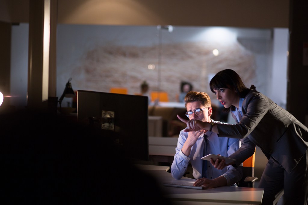 Two government agents are monitoring a computer in the night office using modern technology.